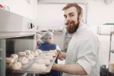 Genç karizmatik fırıncı fırınında fırında ekmek rulo ile bir fırın tepsisi koyar