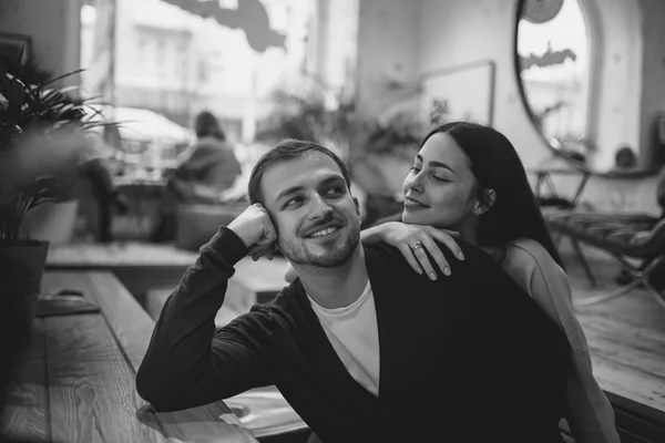 Liebende Mädchen hält ihre Hand auf die Schulter ihres Freundes, der am Tisch im gemütlichen romantischen Café sitzt. Schwarz-Weiß-Foto — Stockfoto