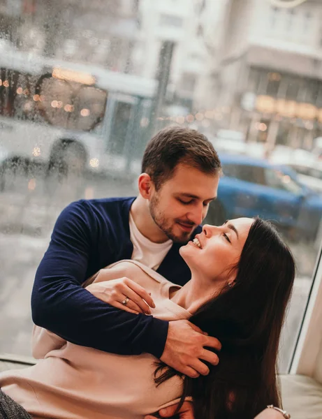 Chico cariñoso abraza a su hermosa novia sentada en el alféizar de la ventana en un acogedor café . —  Fotos de Stock