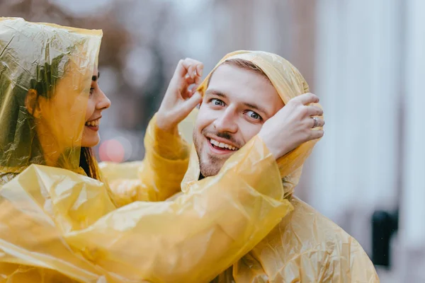 Couple amoureux romantique, gars et sa petite amie vêtus d'imperméables jaunes sont câlins dans la rue sous la pluie — Photo