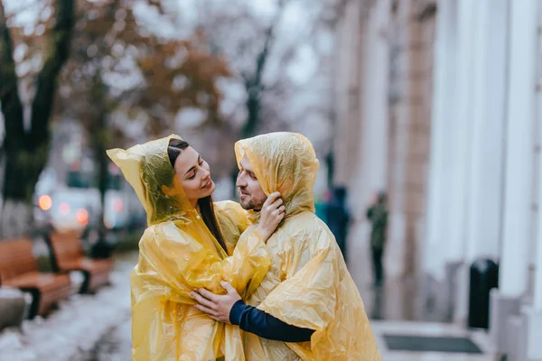 Sevgi dolu çift, adam ve sarı yağmurluklar giymiş kız arkadaşı yağmurda sokakta sarılmak vardır — Stok fotoğraf