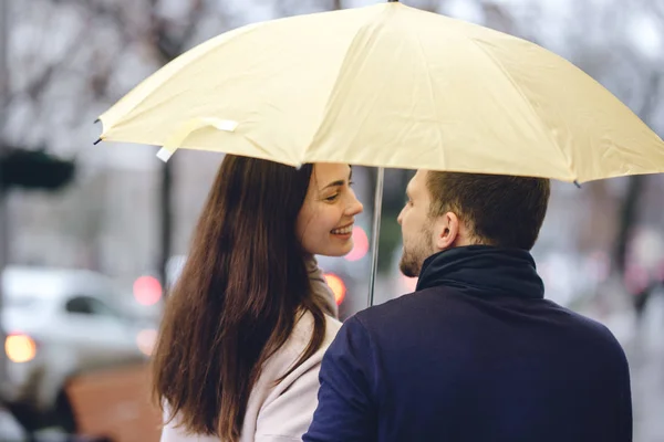 Bella coppia, ragazzo e la sua ragazza vestita con abiti casual stare sotto l'ombrello e guardarsi per strada sotto la pioggia — Foto Stock