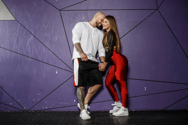 Bonito casal atlético. Menina bonita esbelta e homem atlético forte em roupas esportivas estão abraçando no fundo da parede violeta elegante — Fotografia de Stock