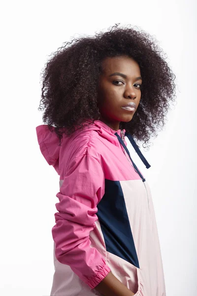 Young curly brown-haired girl dressed in the pink sport jacket stands at the white background in the studio — Stock Photo, Image