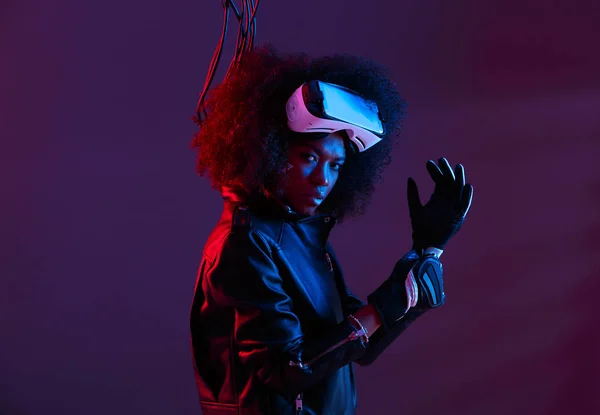 Kudrnaté tmavé vlasy dívka na sobě černou koženou bundu a rukavice nosí brýle virtuální reality na její hlavu v temné studio s neon light — Stock fotografie