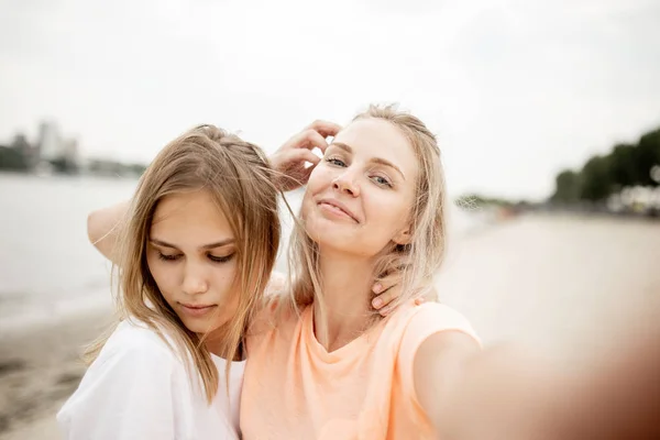 Twee jonge aantrekkelijke blonde meisjes nemen een selfie op het strand op een warme, winderige dag — Stockfoto