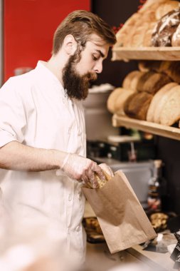 Sakallı ve bıyıklı karizmatik fırıncı fırında bir kese kağıdına taze ekmek koyar