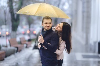 Mutlu romantik çift, adam ve rahat giysiler giymiş kız arkadaşı şemsiye altında sarılma ve yağmurda sokakta birbirlerine bakmak.