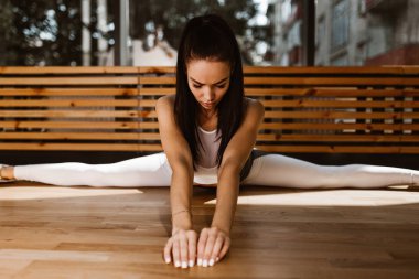 Güzel ince koyu saçlı kız beyaz spor üst ve tayt giymiş spor salonunda böler yapıyor