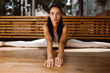Güzel ince koyu saçlı kız beyaz spor üst ve tayt giymiş spor salonunda böler yapıyor
