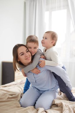 Genç güzel anne ve pijama giymiş iki küçük oğulları hafif rahat yatak odasında yatağın üstüne iyi eğlenceler