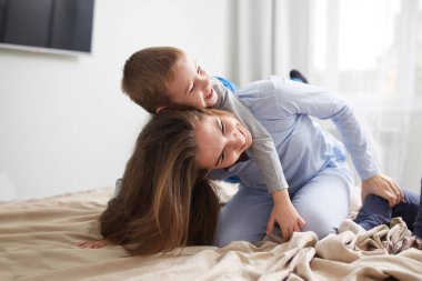 Genç güzel anne ve küçük oğlu pijama giymiş hafif rahat yatak odasında yatağın üstüne iyi eğlenceler