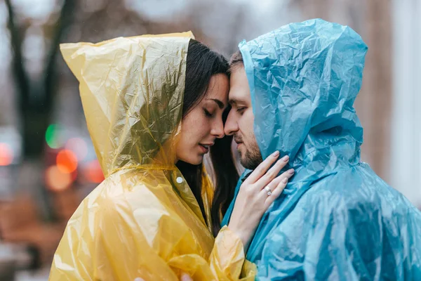 Cara amorosa e sua namorada nas capas de chuva ficar cara a cara na rua na chuva — Fotografia de Stock