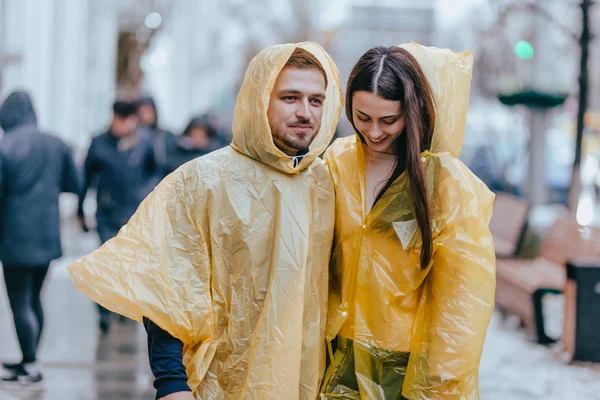 Happy guy and his girlfriend dressed in yellow raincoats are walking on the street in the rain