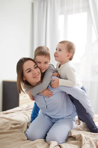 Νέοι όμορφη μητέρα και δύο γιους λίγο ντυμένος με πιτζάμες διασκεδάστε στο κρεβάτι στο φως άνετο υπνοδωμάτιο — Φωτογραφία Αρχείου