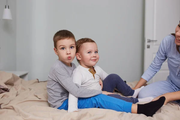 Двоє маленьких братів сидять, обіймаючись на ліжку з бежевою ковдрою у світлій затишній спальні — стокове фото