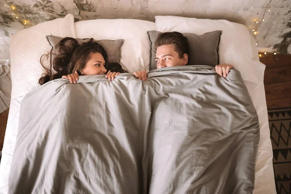 Guy e menina estão deitados na cama sob cobertores cinza e olhar um para o outro — Fotografia de Stock