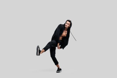 Siyah pantolon giymiş yakışıklı genç dansçı, çıplak gövde üzerinde bir sweatshirt sokak dansı dans ederken bir bacak yukarı kaldırır