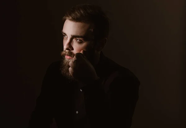 Портрет задумчивого человека с бородой и стильной прической, одетого в черную рубашку на тёмном фоне — стоковое фото