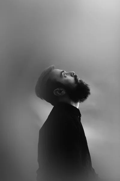 Schwarz-Weiß-Fotoporträt eines stilvollen Mannes im Profil mit Bart im schwarzen Hemd im Nebel — Stockfoto