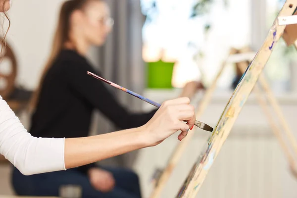 Mão de meninas segura um pincel de pintura. Processo de pintura quadro nos cavaletes no estúdio de arte — Fotografia de Stock