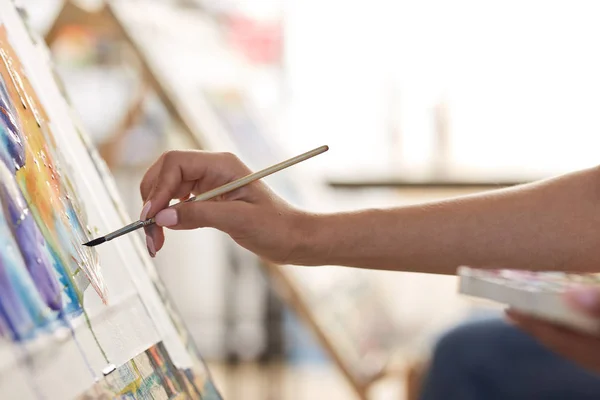 Mão de meninas segura um pincel de pintura. Processo de pintura quadro nos cavaletes no estúdio de arte — Fotografia de Stock