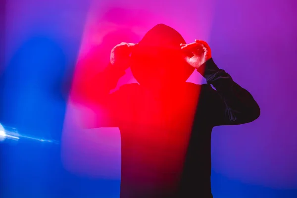 Ritratto di uomo di moda in maglione nero con cappuccio e occhiali da sole in luce al neon in studio — Foto Stock