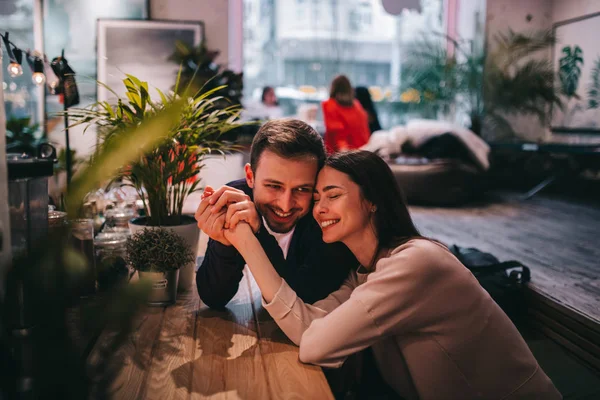 Glücklich liebender Kerl hält seine Freundinnen an der Hand, die am Tisch im Café sitzen und schaut sie an. — Stockfoto