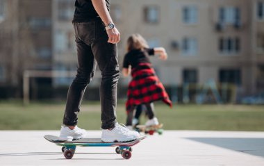 Genç baba ve oğlu şık günlük kıyafetler giyip güneşli bir günde evin yanındaki platformda kaykay sürerler.