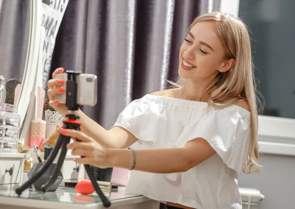 Красива дівчина-блогер встановлює телефон на підставку на туалетний столик для зйомок відео для її блогу — стокове фото