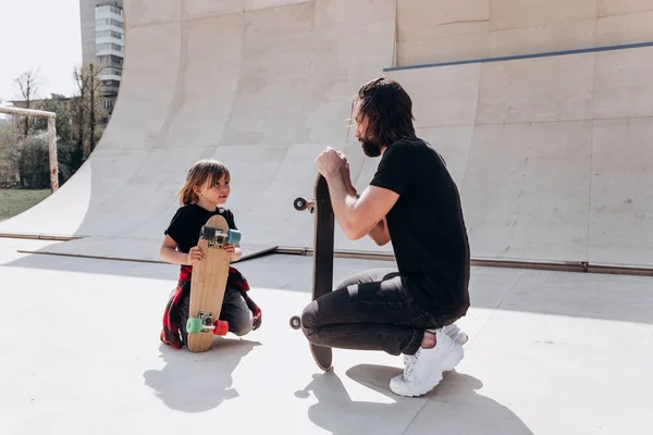 Vader en zijn zoon gekleed in de casual kleding zijn plaatsings naast de Skateboards in een skatepark op de zonnige dag — Stockfoto