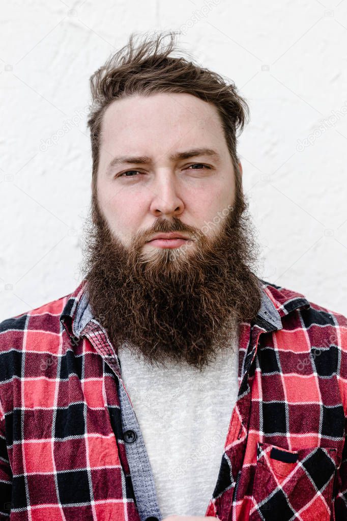The portrait of the strong brutal man with a beard dressed in a checked shirt on the white background