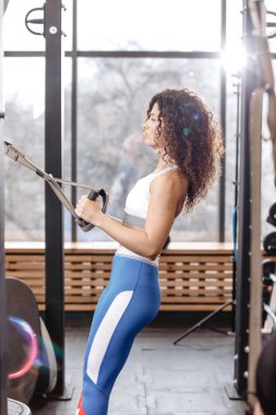 Bir spor giyim giyinmiş atletik kıvırcık kız Trx egzersiz modern spor salonunda güneş ışığında tam vardır.