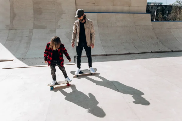 Jonge vader en zijn zoon rijden Skateboards in een skatepark met glijbanen buiten op de zonnige dag — Stockfoto