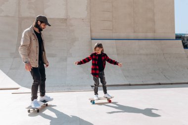 Baba ve onun küçük oğlu Casual giysi binmek kaykaylar içinde güneşli bir gün içinde slaytlar ile bir paten parkında giyinmiş