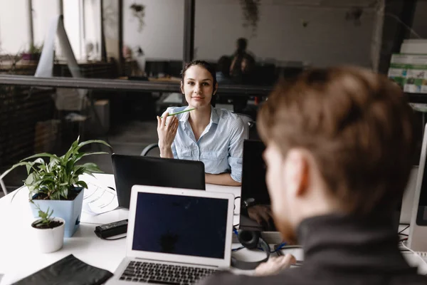 Femeia tânără și tipul îmbrăcat în haine în stil de birou lucrează la laptopurile care stau la birouri în biroul modern ușor echipat cu echipamente moderne de birou — Fotografie, imagine de stoc