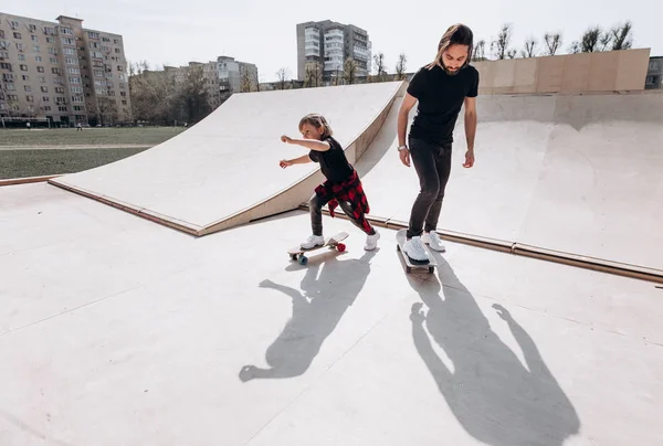 Vader en zijn kleine zoon gekleed in de casual kleren Ride Skateboards in een skatepark met glijbanen op de zonnige dag — Stockfoto