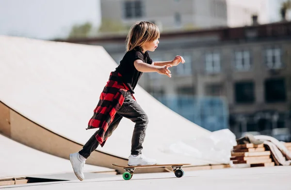 Grappige jongen gekleed in de stijlvolle casual kleding ritten skateboard op een platform buiten naast het huis op de zonnige warme dag — Stockfoto
