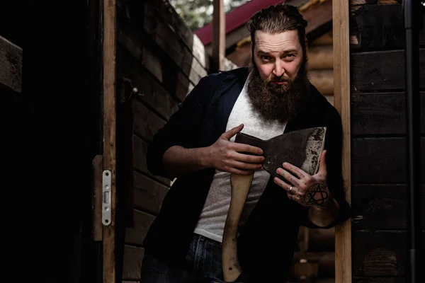 Brutal homme fort avec une barbe vêtue de vêtements décontractés tient la hache dans ses mains debout dans la porte — Photo