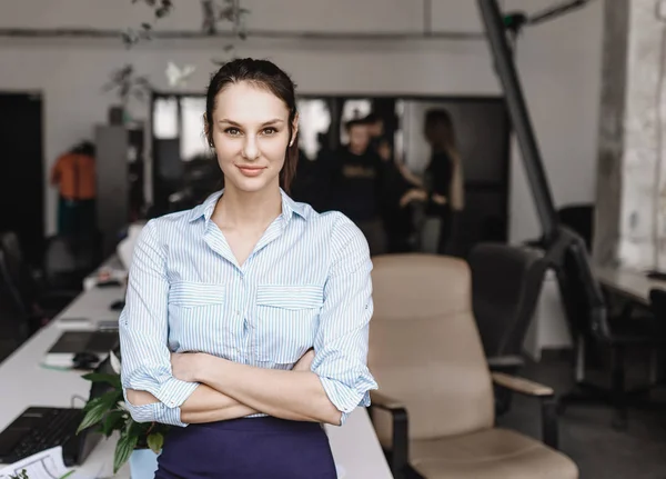 Glimlachende jonge brunette meisje gekleed in kantoor stijl kleding staat in het moderne kantoor — Stockfoto