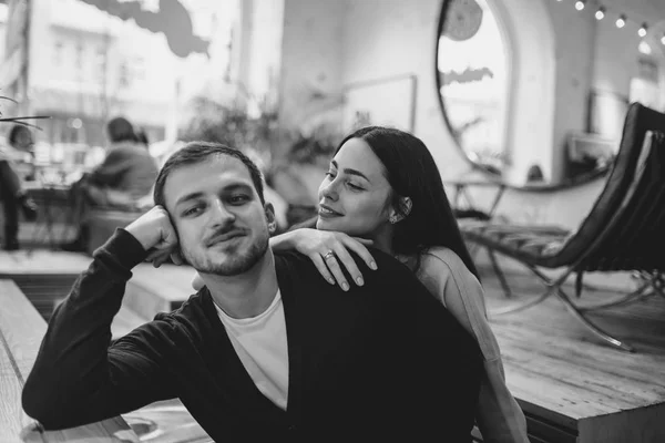 Chica cariñosa sostiene su mano en el hombro de su novio sentado a la mesa en el acogedor café romántico. Foto en blanco y negro — Foto de Stock