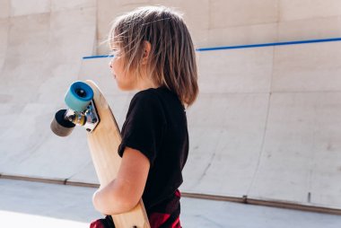 Elinde kaykay ile rahat giysiler giymiş çocuk dışarıda güneşli bir gün içinde slayt yanında bir paten parkta duruyor