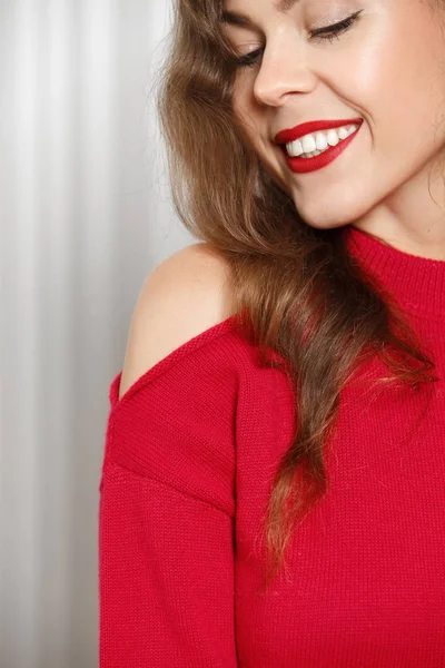 Menina encantadora elegante com batom vermelho vestido com uma camisola vermelha posa contra uma parede branca na sala — Fotografia de Stock
