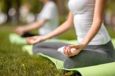 İnce kızlar sıcak bir günde parkta yeşil çim üzerinde yoga paspaslar yoga yapan lotus pozisyonlarda oturup