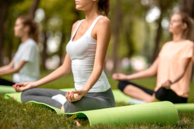 Üç genç ince kız sıcak bir günde parkta yeşil çim yoga paspaslar yoga yapıyor kapanış gözleri ile lotus pozisyonlarda oturup