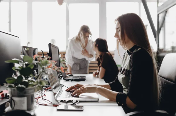 Unge, vakre kvinner i kontorklær jobber på pultene med datamaskin og bærbare PC-er i et moderne, åpent romkontor. – stockfoto