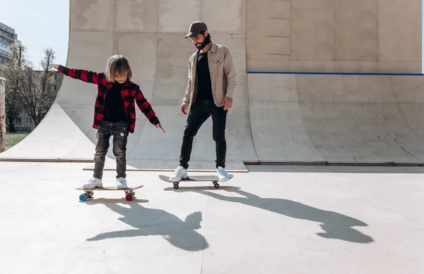 Jonge vader en zijn zoon rijden Skateboards in een skatepark met glijbanen buiten op de zonnige dag — Stockfoto