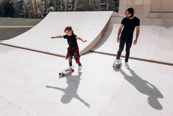 Happy Father en zijn kleine zoon gekleed in de casual kleren Ride Skateboards in een skatepark met glijbanen op de zonnige dag — Stockfoto