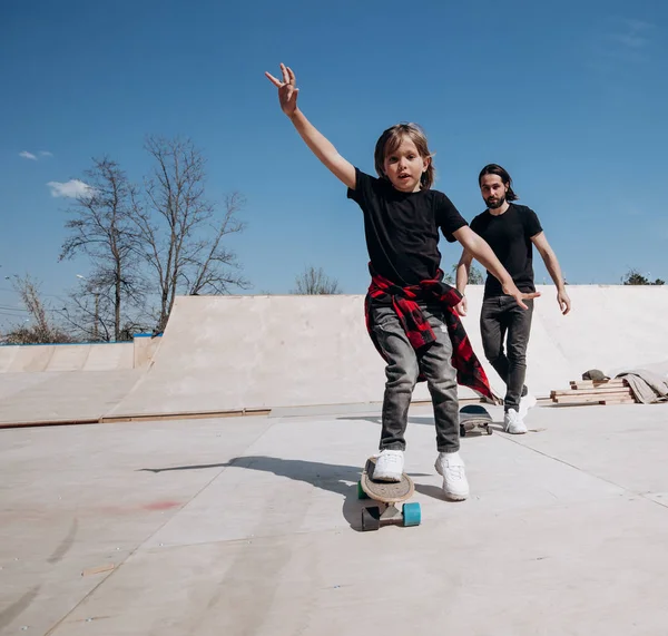아버지와 그의 작은 아들은 캐주얼 한 옷을 입고 스케이트 보드를 타고 화창한 날에 야외 슬라이드와 스케이트 공원에서 재미를 — 스톡 사진
