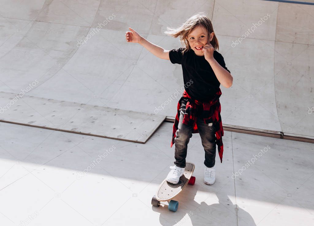 The boy dressed in the casual clothes ride skateboard in a skate park at the sunny warm  day